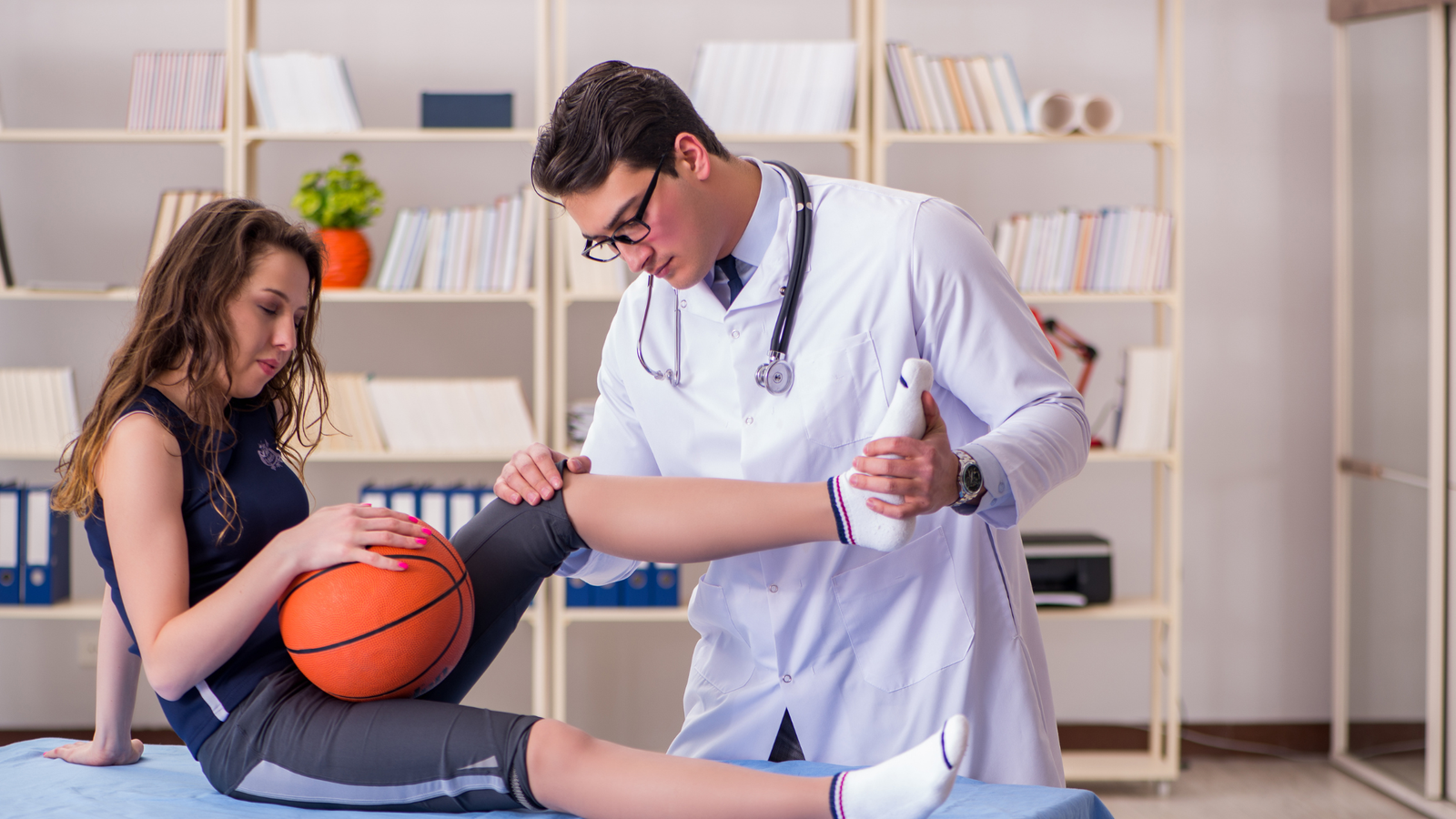 Médico examinando la rodilla de una paciente con una pelota de baloncesto.